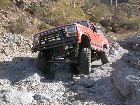1984 Ford Bronco - Modified Ford Bronco tackling a challenging off-road course in a desert environment.