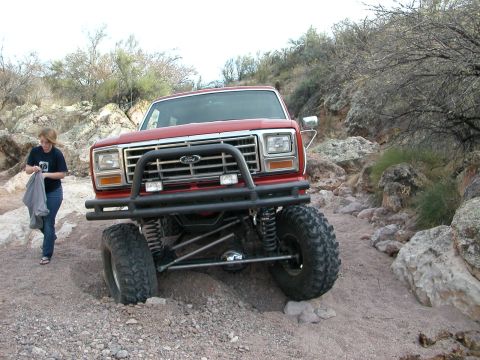 1984 Ford Bronco - This lifted Ford pickup navigates a rough, rocky terrain with a woman standing nearby.