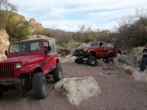 1984 Ford Bronco - Two modified off-road vehicles navigate a desert canyon with rocky terrain.