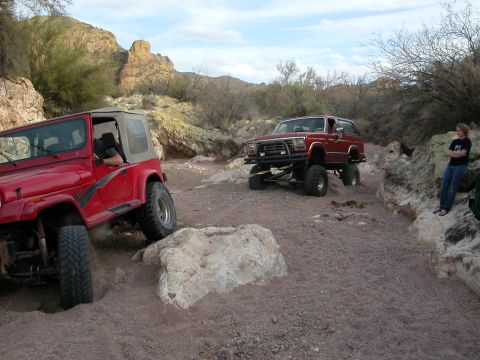 1984 Ford Bronco - A red Ford Bronco tackles a challenging off-road course in a rocky, arid landscape.