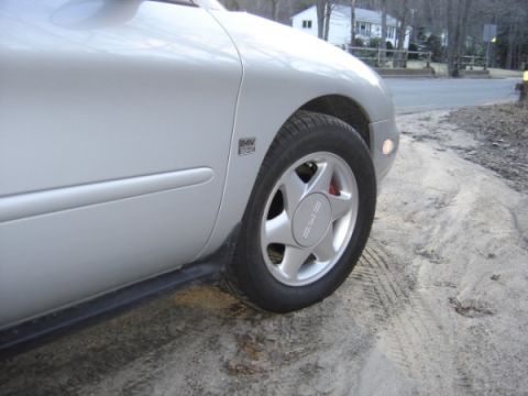 1999 Ford Taurus - Close-up of a silver car's wheel and fender, a five-spoke design and a '24V' badge.