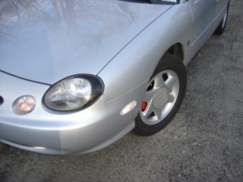 1999 Ford Taurus - The front quarter panel and wheel of a silver sedan are visible in this close-up shot.