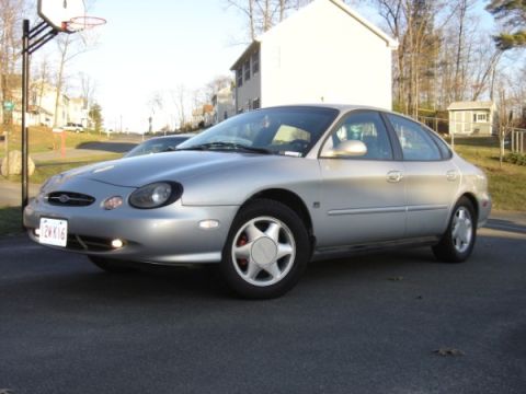 1999 Ford Taurus - A silver sedan is parked on an asphalt surface with houses in the background.