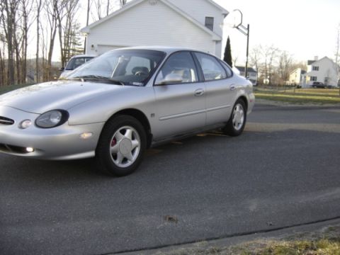 1999 Ford Taurus - A silver sedan is parked on a street in front of a house, showing its front 3/4 view.