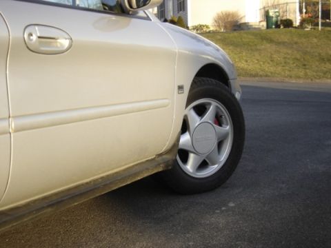 1999 Ford Taurus - Close-up view of a beige sedan's side and alloy wheel, showing a red brake caliper.