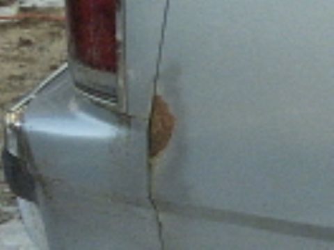 1991 Ford LTD Crown Victoria - Close-up of the rear quarter panel of a silver sedan beside the red vertical tail lamp, showing a large patch of orange rust bubbling throu…
