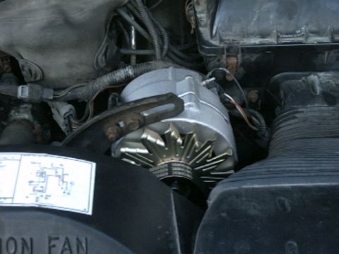 1991 Ford LTD Crown Victoria - Close-up view of an alternator and associated engine components, with a diagram sticker visible on the fan shroud.