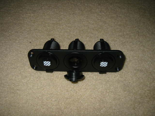 Black triple switch panel with two illuminated symbols and one central socket