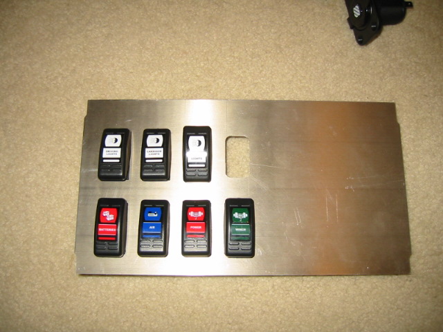Metal panel with eight aftermarket switches installed. Some switches have labels like 'DIMMING LIGHTS', 'BATTERY', 'POWER', and 'WINCH'
