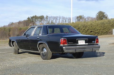 1991 Ford Crown Victoria - Rear view of a black sedan with a license plate reading 26P R35, parked outdoors on a gravel surface.
