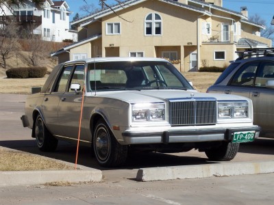 1972 Ford Ranchero - This white sedan, likely from the early 1980s, features a distinctive vertical grille and is parked alongside another car.