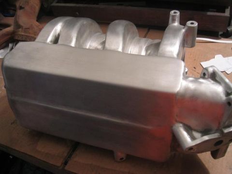 1986 Ford Bronco - A clean aluminum intake manifold sits on a wooden surface, ready for installation.