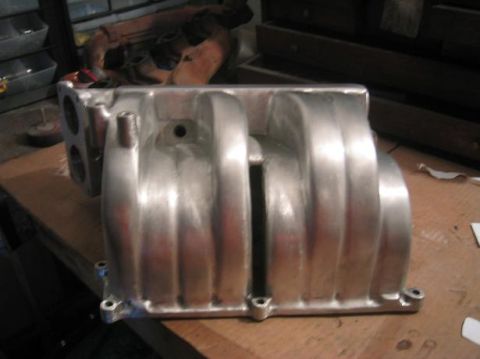 1986 Ford Bronco - An aluminum intake manifold with a ribbed design is shown on a workbench.