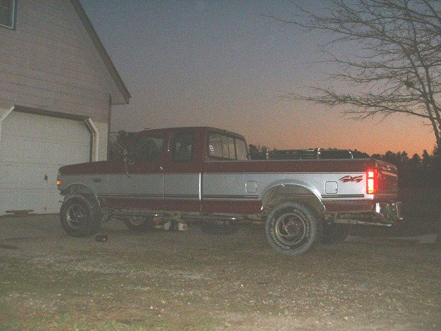 Two-tone red and silver extended-cab pickup parked by a house at dusk