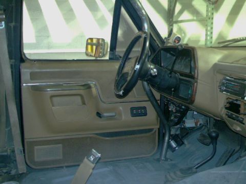 1989 Ford Bronco - The interior of a truck shows the driver's side door panel, steering wheel, and dashboard with a roll cage installed.