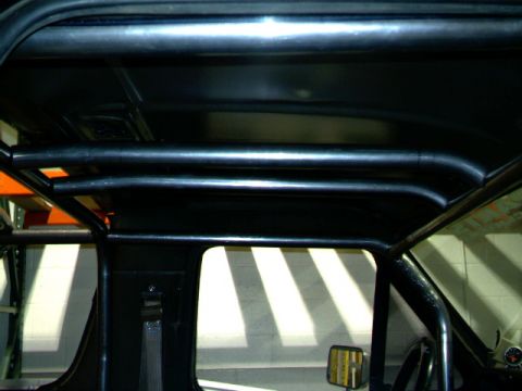 1989 Ford Bronco - The interior of a vehicle shows a custom black roll cage structure overhead and along the sides.