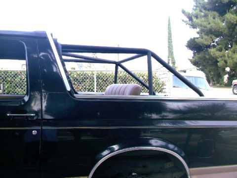 1989 Ford Bronco - Side view of a black Ford Bronco with a roll cage and a tan seat visible.