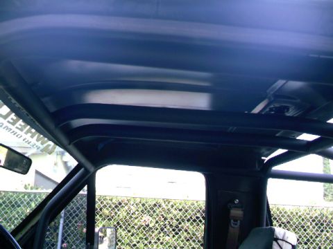 1989 Ford Bronco - The interior of a vehicle shows a prominent roll cage structure, with a side mirror and a sticker displaying text visible.