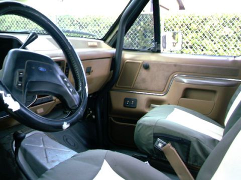 1989 Ford Bronco - The interior of a vehicle, a steering wheel, door panel, and seat with a visible roll cage.