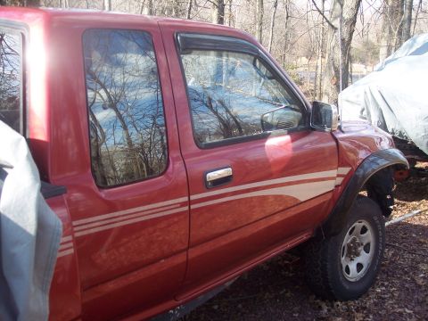 1995 Toyota Tacoma - The side of a red pickup truck is shown, with trees reflected in the windows.