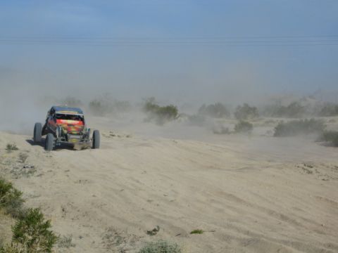 Red off-road buggy raising a wheel over a sandy berm in dusty desert