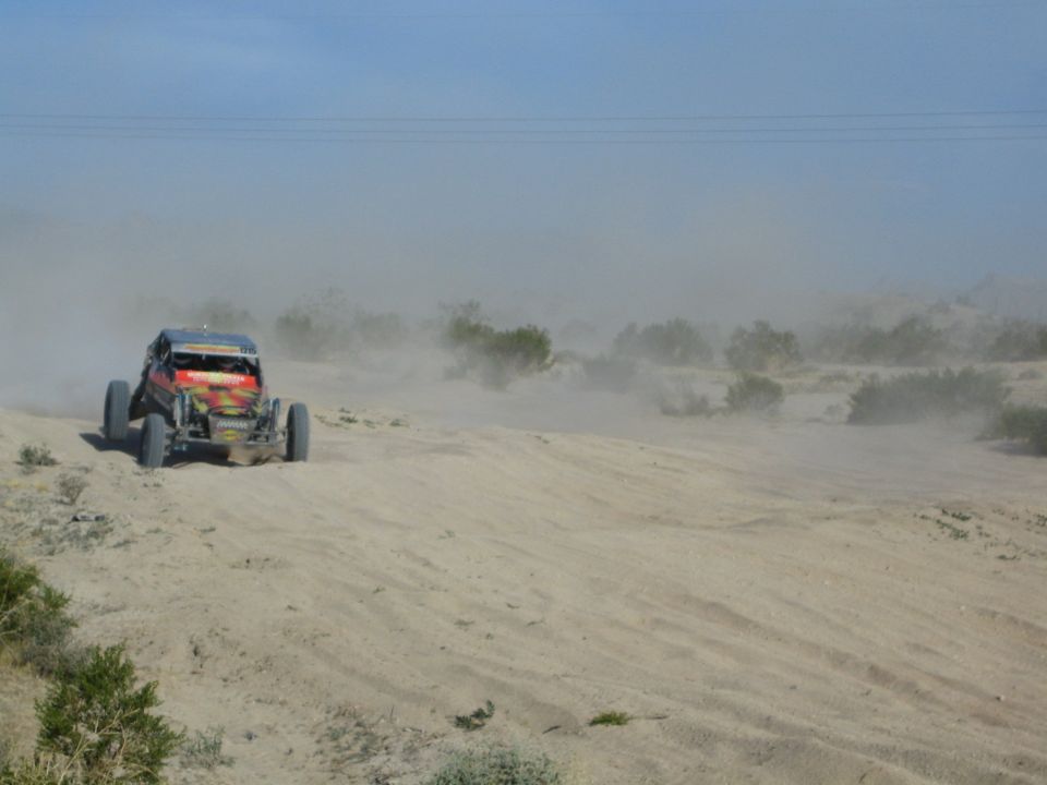 Red off-road buggy raising a wheel over a sandy berm in dusty desert