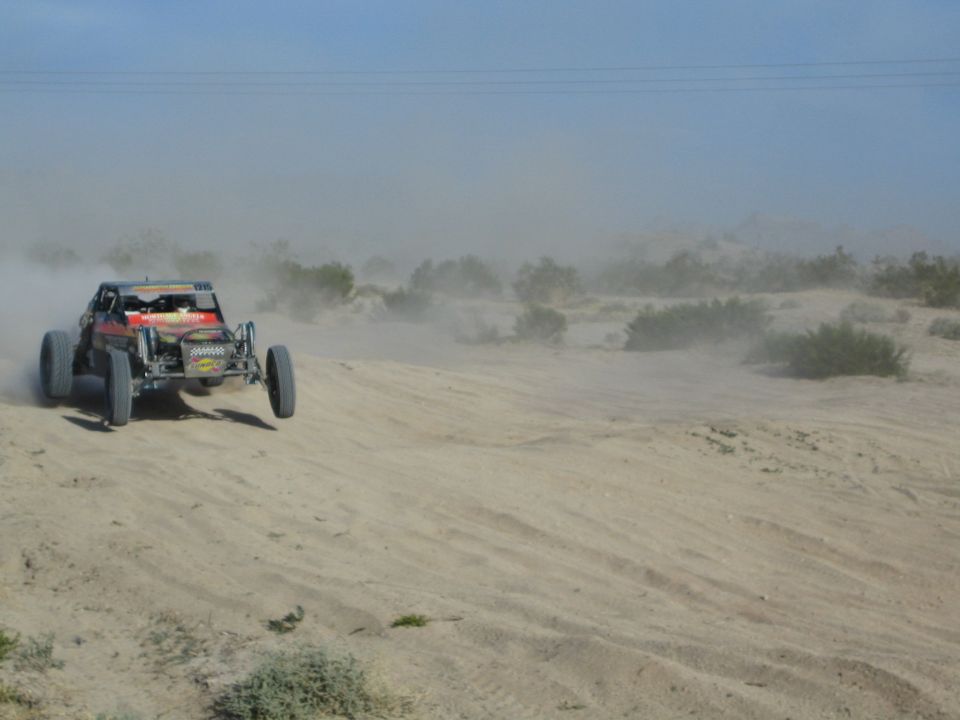 Red and black off-road buggy with raised front wheel on a dusty desert track