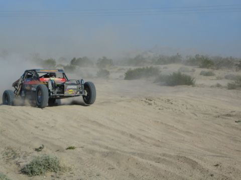 Orange and black off-road buggy with a winch climbing a sandy desert berm