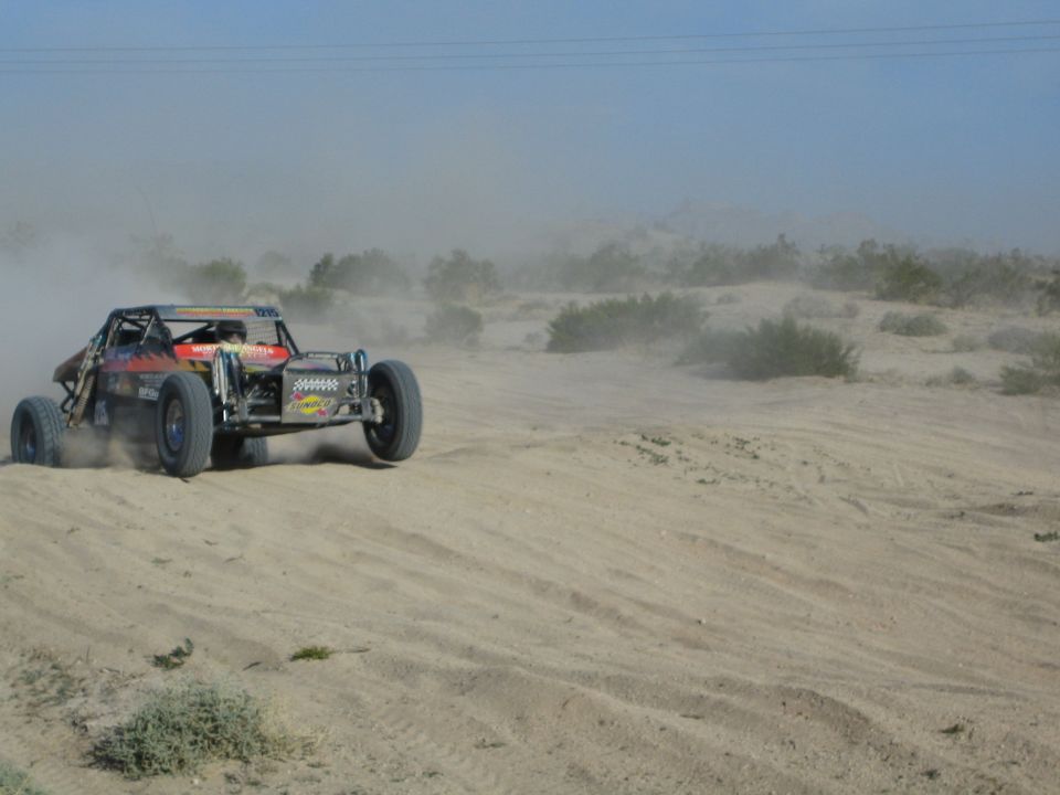 Orange and black off-road buggy with a winch climbing a sandy desert berm