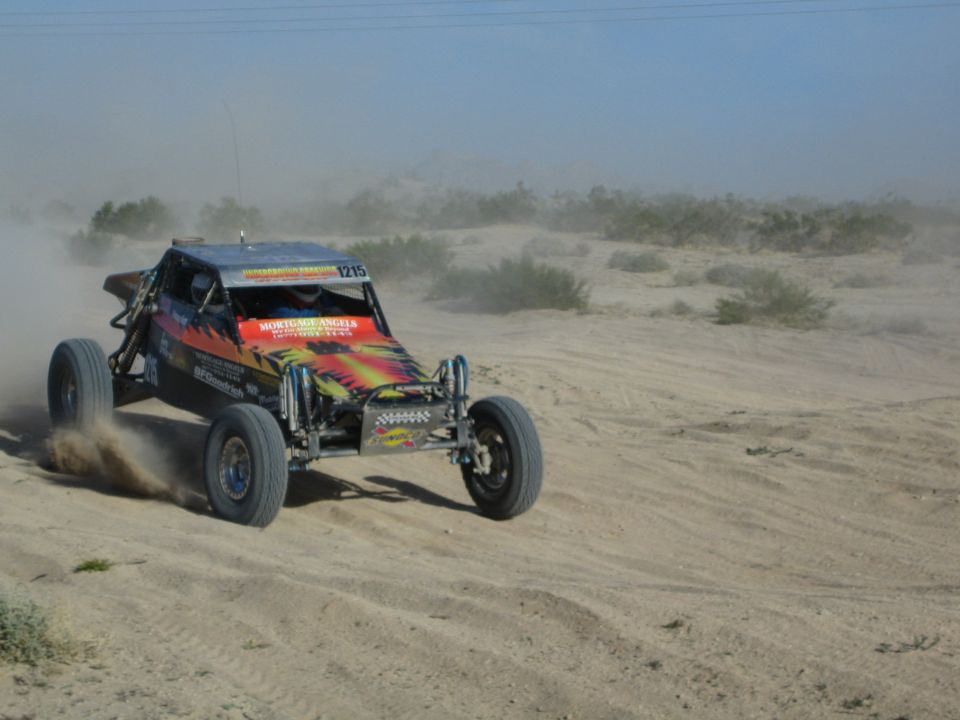 Number 1215 colorful off-road race buggy throwing sand on a desert course