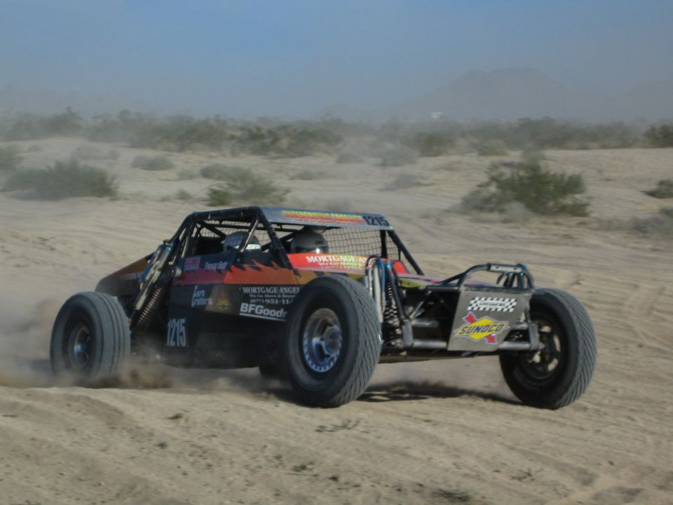 Off-road buggy number 1215 powering through a turn in a dusty desert