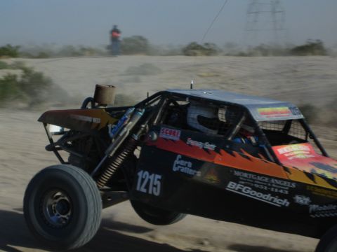 Black off-road buggy number 1215 racing past power lines in the desert