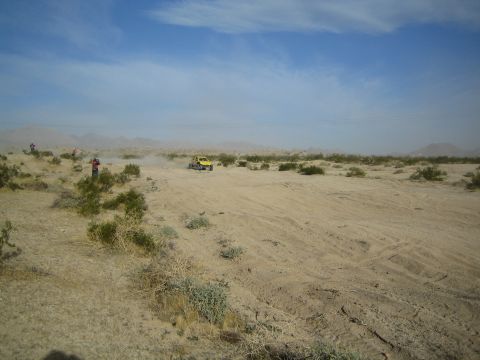 Distant yellow off-road buggy in vast open desert under a blue sky