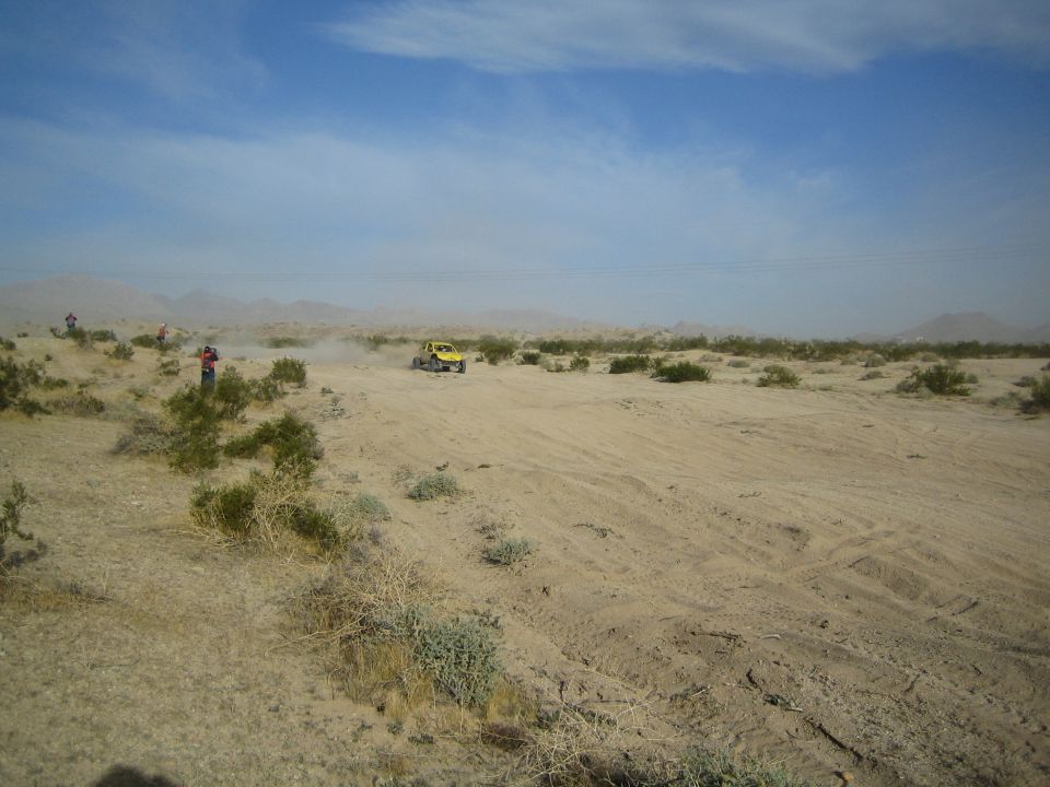 Distant yellow off-road buggy in vast open desert under a blue sky