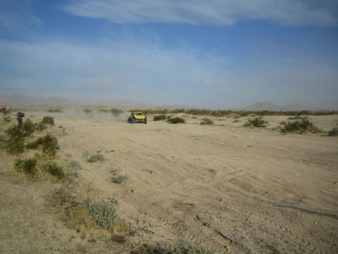 Yellow off-road buggy crossing open desert scrub under a hazy sky