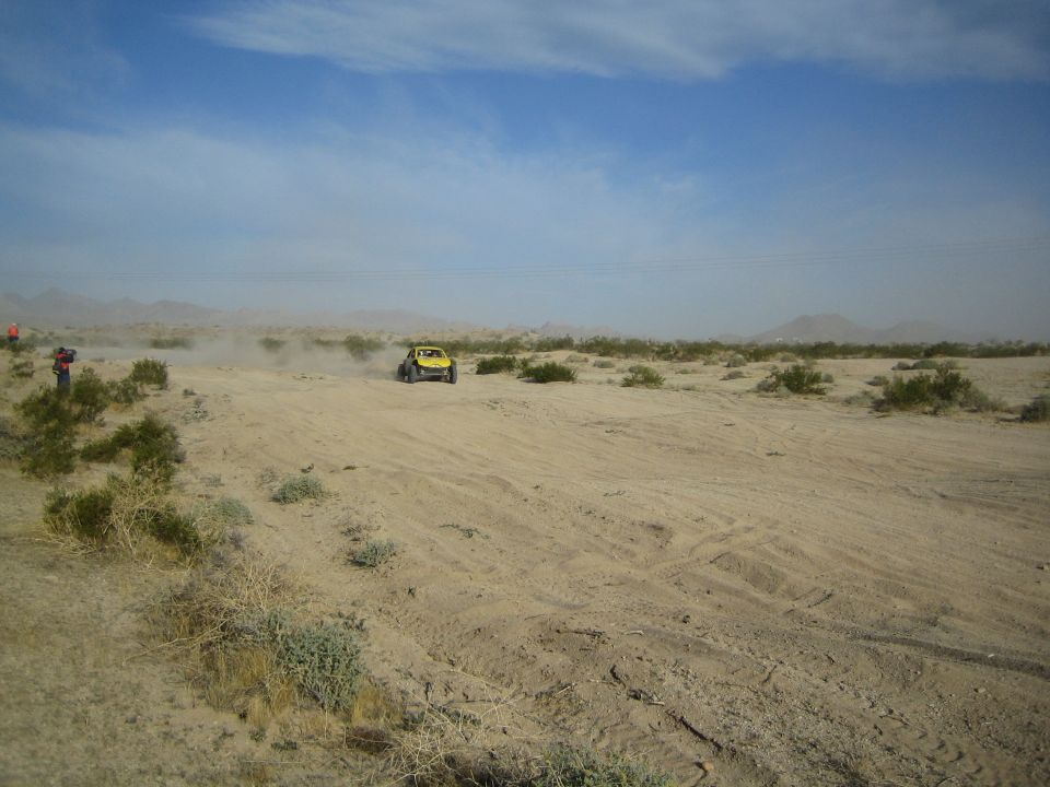 Yellow off-road buggy crossing open desert scrub under a hazy sky