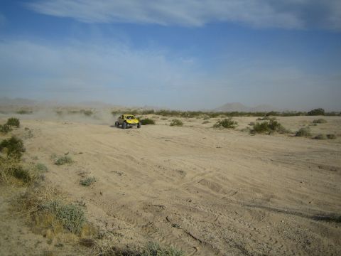 Yellow off-road buggy crossing sandy desert with power lines in distance