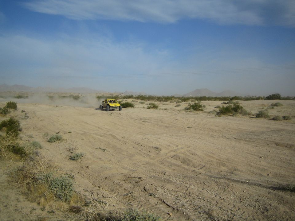 Yellow off-road buggy crossing sandy desert with power lines in distance
