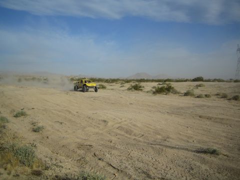 Yellow off-road buggy raising a wheel over a sandy desert rise