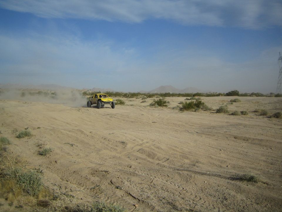 Yellow off-road buggy raising a wheel over a sandy desert rise