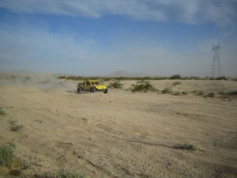 Yellow off-road buggy crossing desert sand near a power transmission tower