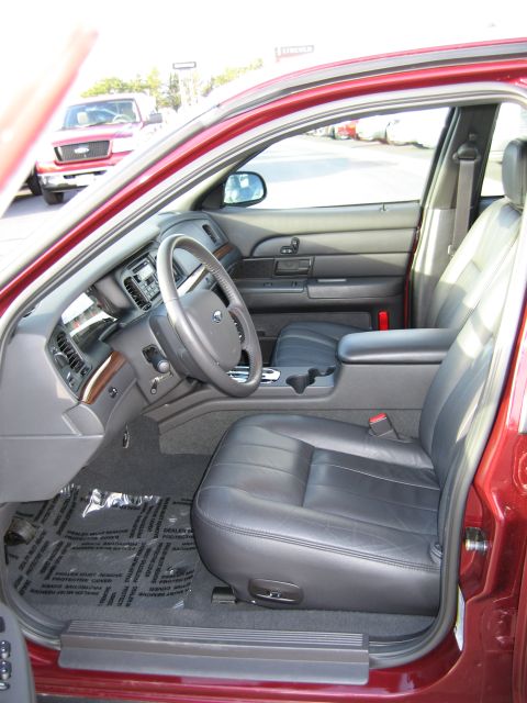 2005 Ford Crown Victoria - The interior of a red sedan features black leather seats and a clean dashboard. A red pickup truck is parked outside.