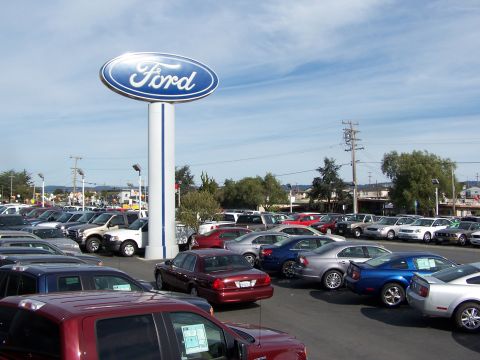 2005 Ford Crown Victoria - A wide view of a Ford dealership lot filled with various vehicles under a partly cloudy sky.