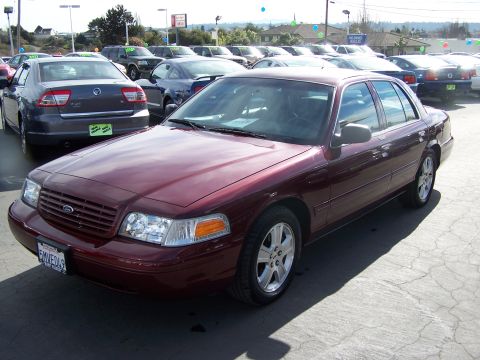 2005 Ford Crown Victoria - A maroon sedan is parked in a lot with other vehicles visible in the background under a bright sky.