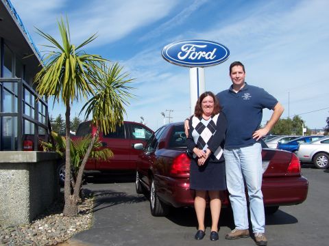 2005 Ford Crown Victoria - A couple poses with a maroon Ford Crown Victoria in front of a Ford dealership sign.