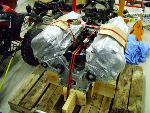 2003 Ford Mustang - Engine on a wooden pallet, wrapped in plastic and secured with red straps, with a red ATV in the background.