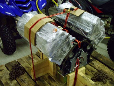 2003 Ford Mustang - Engine block wrapped in plastic and secured to a wooden pallet with red straps, with a blue ATV visible in the background.