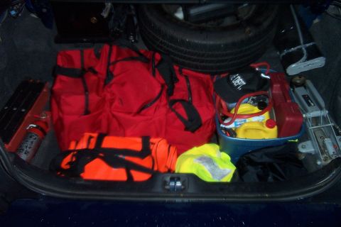 1998 Ford Crown Victoria - Open trunk of a dark blue sedan packed as a first-responder kit: a large red gear duffel and orange harness bag, a yellow high-visibility v…