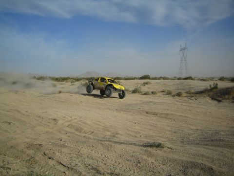 Yellow off-road buggy kicking up dust on desert sand below power lines
