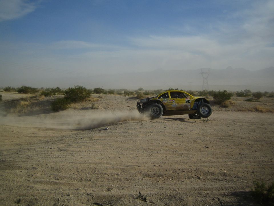 Yellow number 502 Beetle-bodied off-road buggy sliding through desert dust
